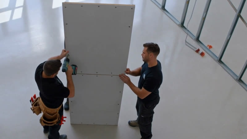 Installer screwing a plasterboard sheet in place while a colleague holds it